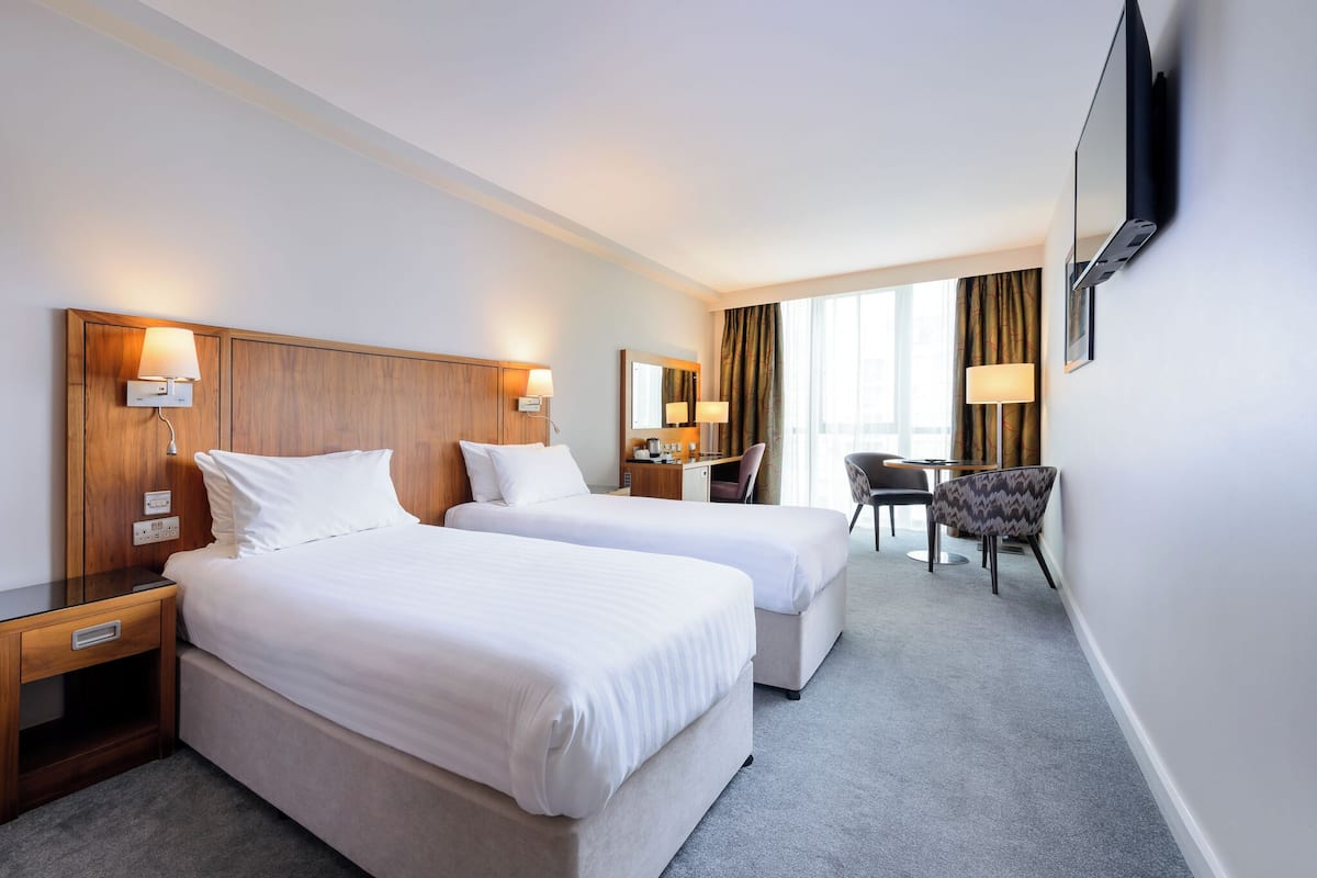 A hotel room with two beds, a desk, a chair, and a TV mounted on the wall.