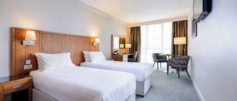 Une chambre d’hôtel avec deux lits, un bureau, une chaise et un téléviseur fixé au mur.