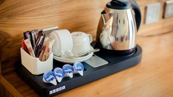 A tray with a coffee maker, a white mug, a plate with a spoon, and a container holding chocolate bars and milk cartons.