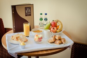Bandeja de desayuno con tostadas, fruta, croissants y jugo sobre una mesa.