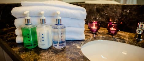 A bathroom with a sink, stacked white towels, and three bottles of body wash and shampoo.