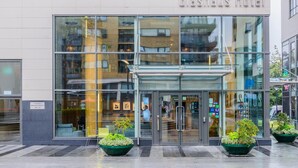 The exterior of the Glasshaus Hotel with a modern glass facade, a visible entrance, and potted plants at the entrance.