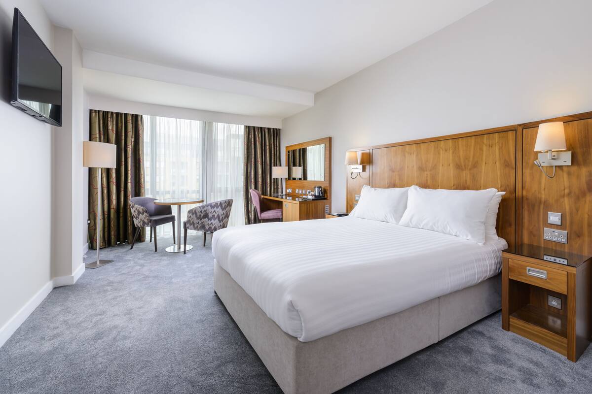 A hotel room with a large bed, a desk with a chair, a TV, and a window with curtains.