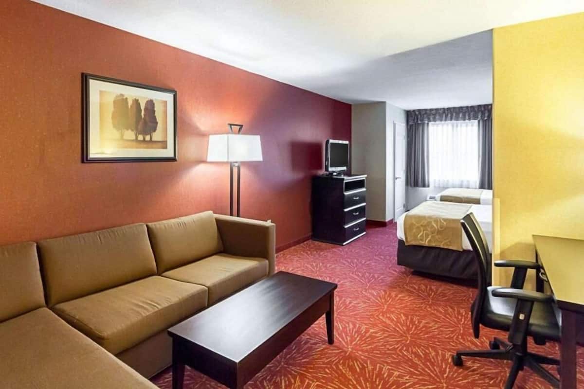 A hotel room with a sofa, a desk, a television, a bed, and a picture on the wall.