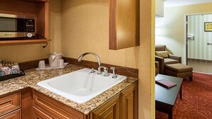 A hotel room with a kitchen area featuring wooden cabinets, a microwave, a sink, and a countertop.