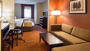 A hotel room with a bed, a desk with a chair, a sofa, a TV, and a lamp.