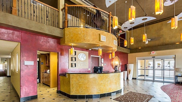 A hotel lobby with a reception desk, a check-in counter, a staircase, and a large open space with patterned carpet.