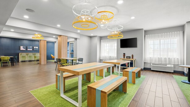 A modern conference room with wooden tables, benches, and a green carpet. - Spark by Hilton Stillwater (Stillwater)