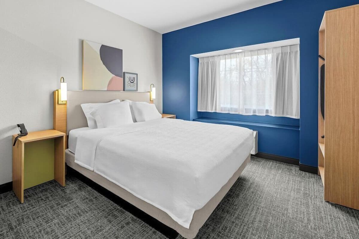 A hotel room with a bed, bedside tables, a window with curtains, and a wall with artwork.