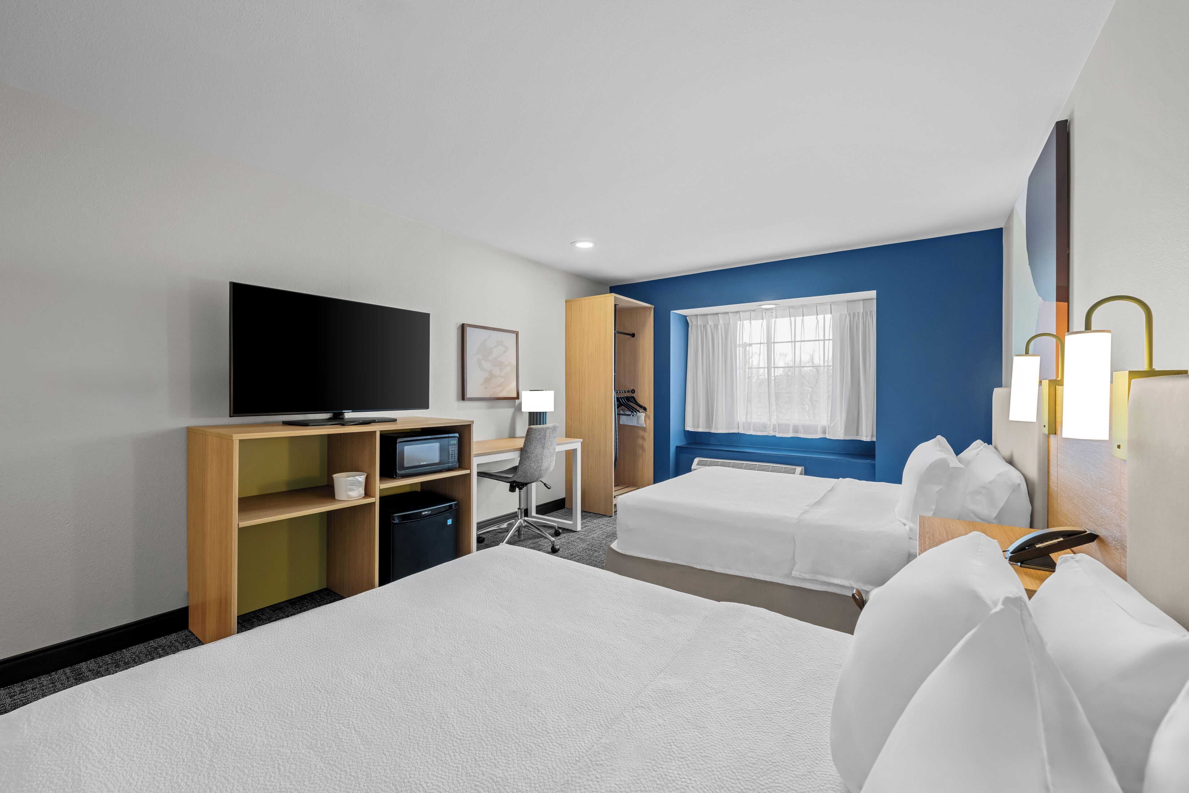 A hotel room with two beds, a desk with a computer, a television, and a window with curtains.