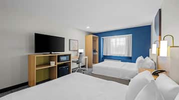 A hotel room with two beds, a desk with a computer, a television, and a window with curtains.