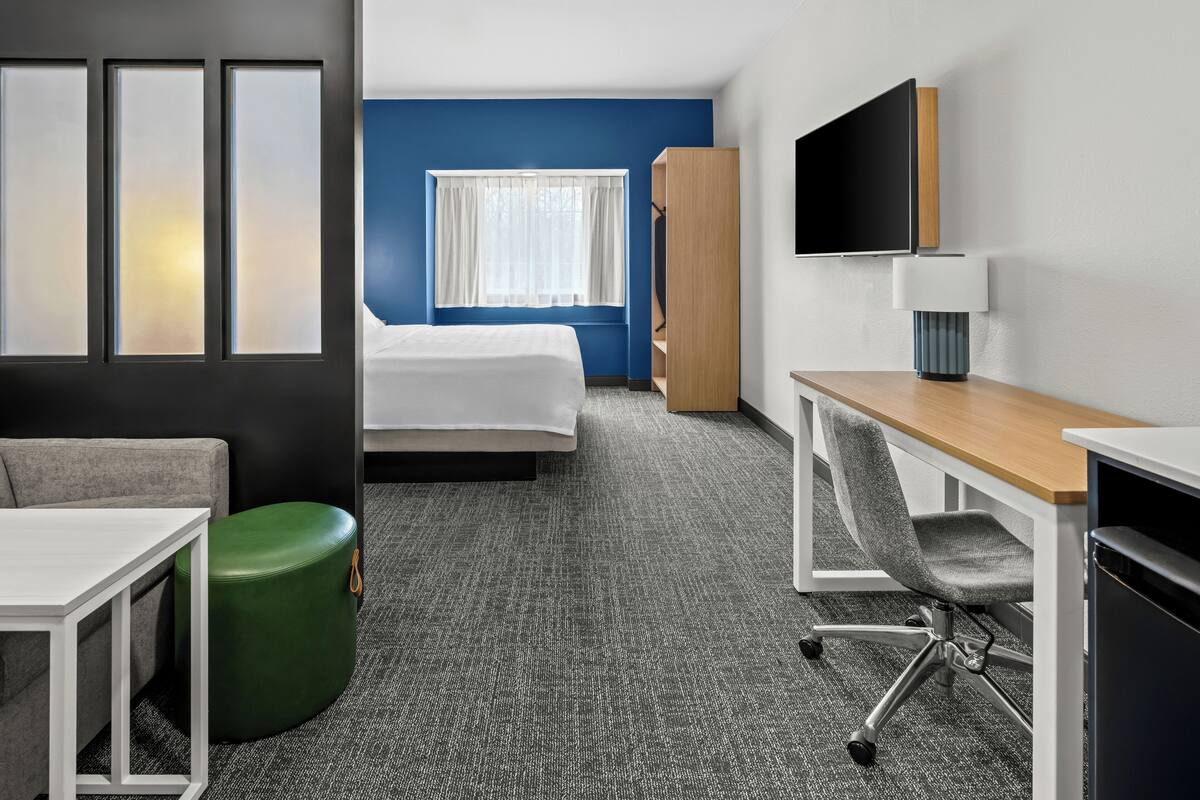 A hotel room with a bed, a desk, a chair, a TV, and a wardrobe.