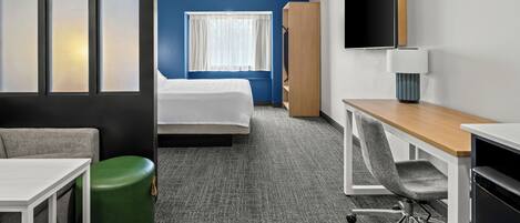 A hotel room with a bed, a desk, a chair, a TV, and a wardrobe.