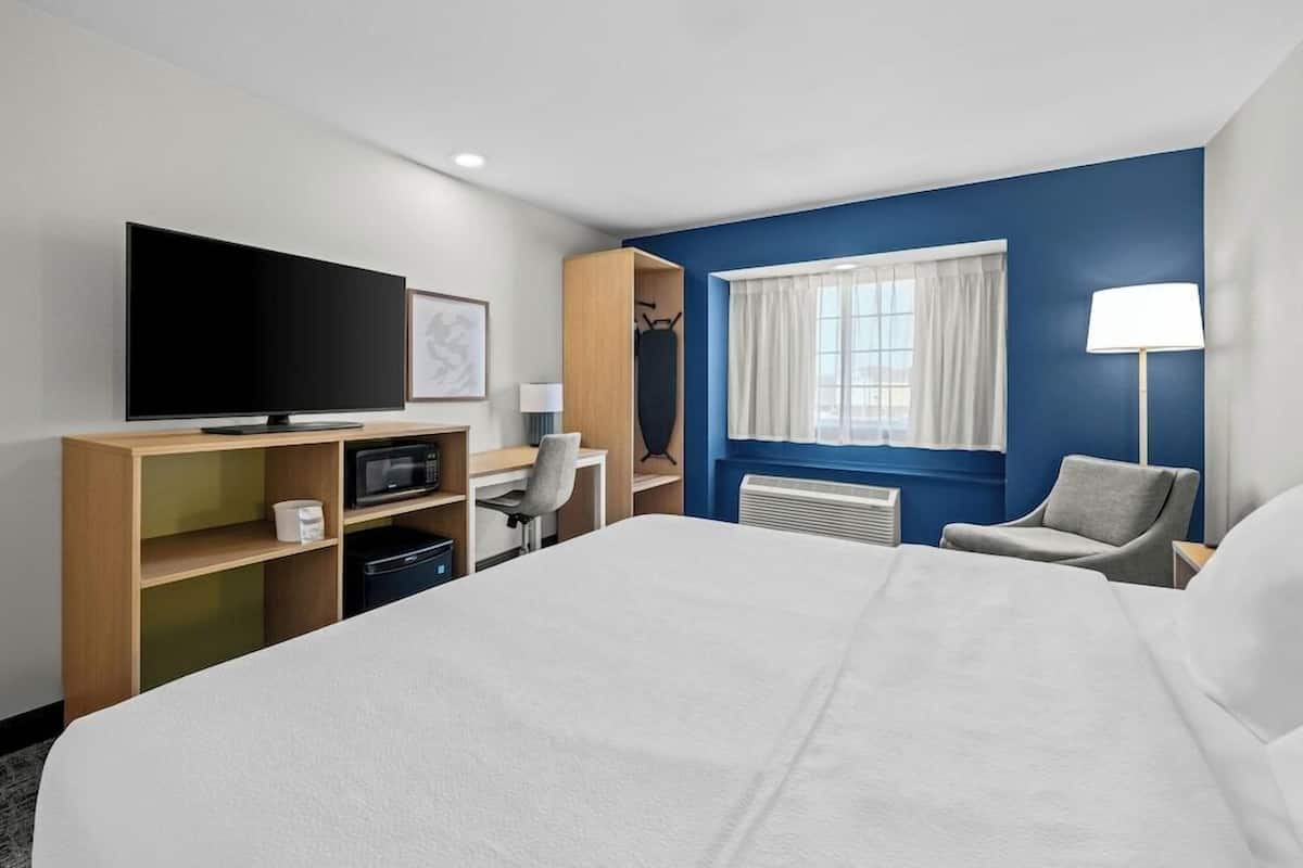 A hotel room with a bed, a TV, a desk with a chair, a lamp, and a window with curtains.
