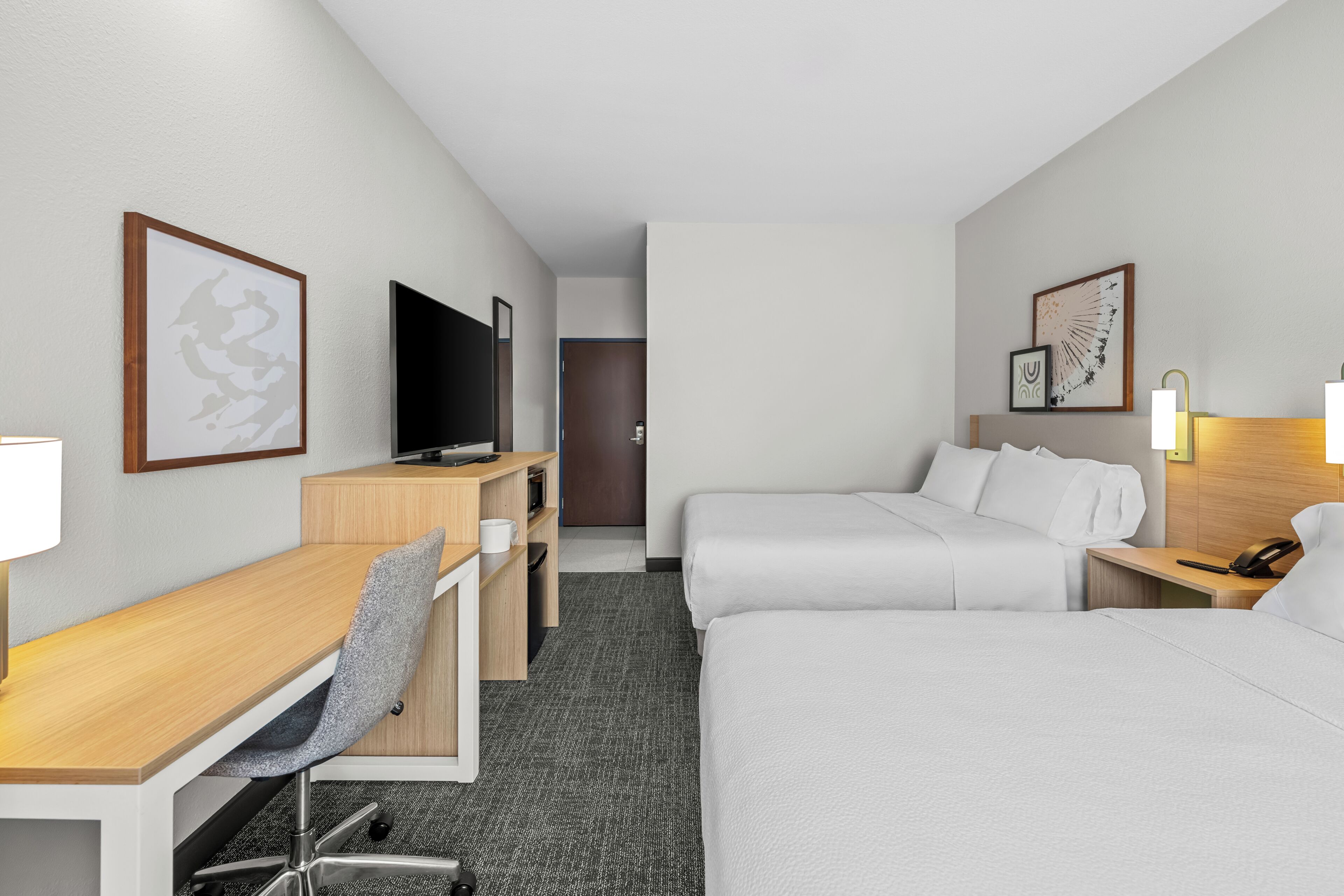 Habitación de hotel con escritorio, dos camas, televisión y obras de arte en las paredes.