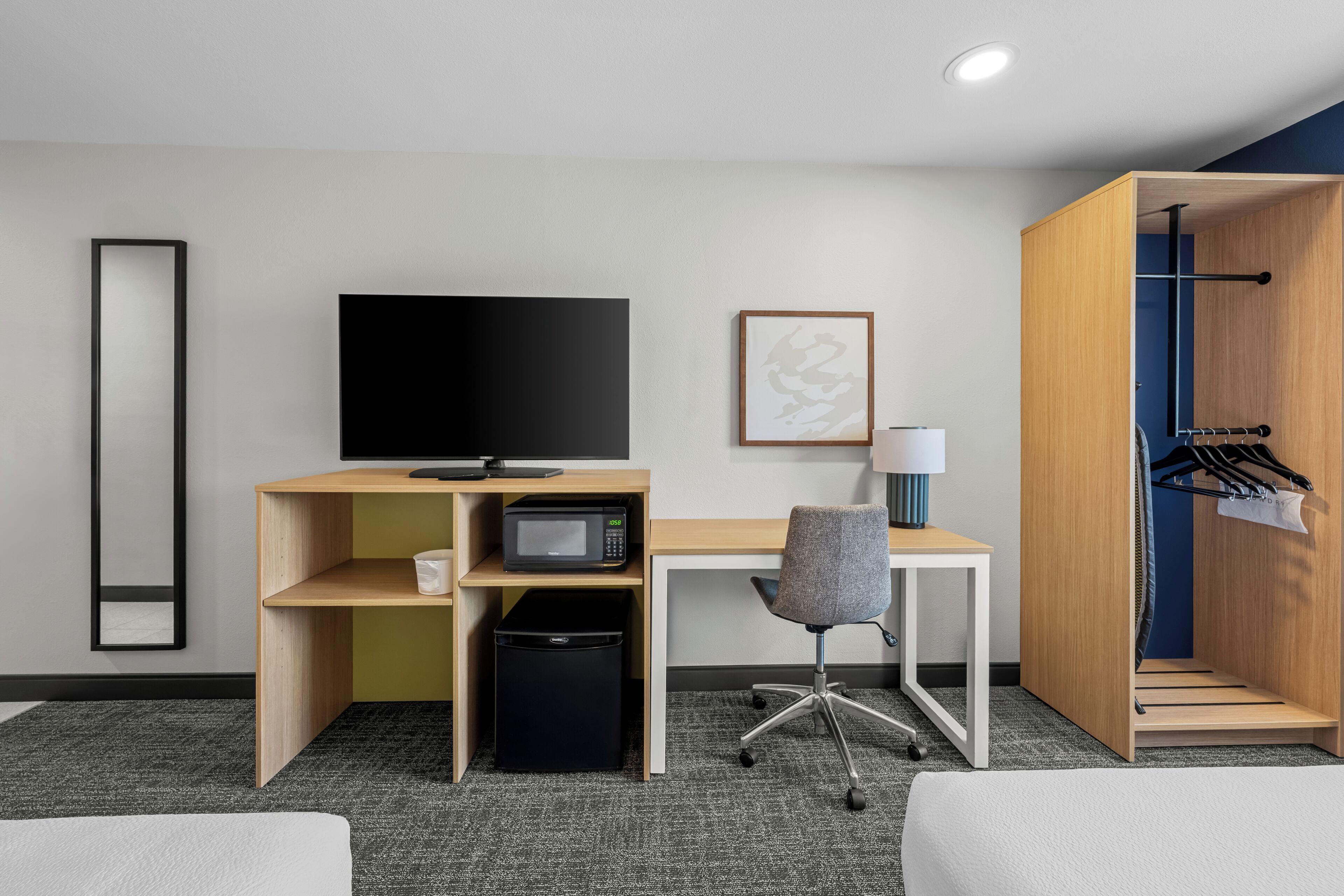 A hotel room with a desk, a television, a microwave, a trash bin, a chair, a coat rack, and a bed.