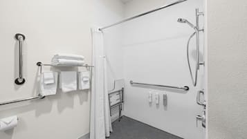 Un baño con ducha, barras de apoyo, toallero y dispensador de papel higiénico.
