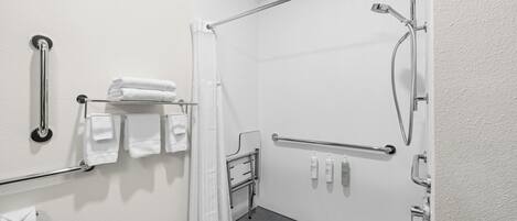 A bathroom with a shower, grab bars, a towel rack, and a toilet paper dispenser.