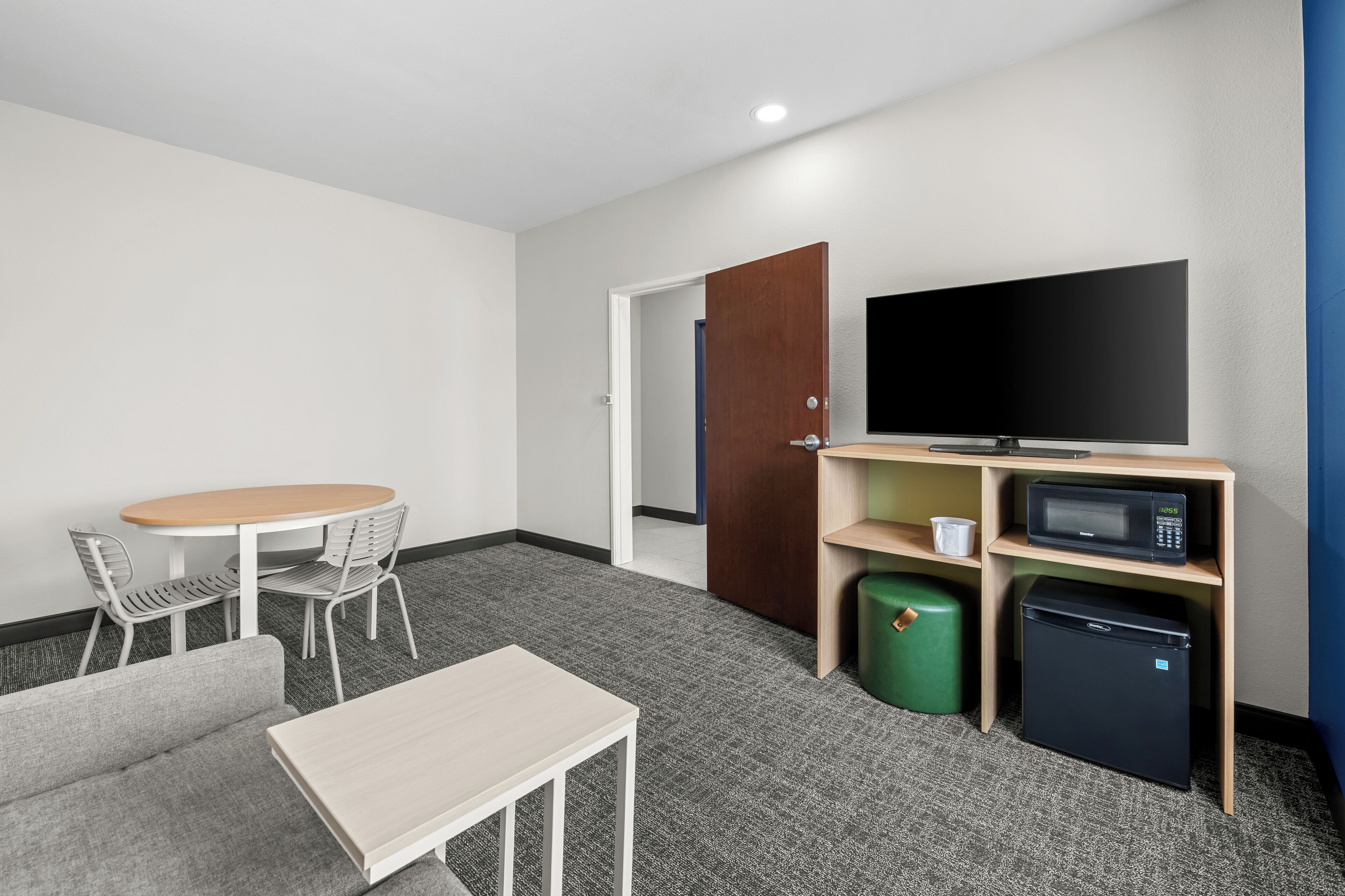 A hotel room with a sofa, a small table, a TV, a microwave, a mini fridge, and a trash bin.
