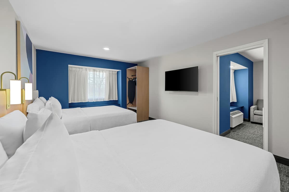 Habitación de hotel con dos camas, televisión, ventana con cortinas y puerta que da a un baño.