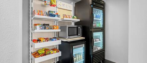 Eine kompakte Küchenzeile mit Mikrowelle, Minikühlschrank und einer Regalausstattung mit Snacks und Getränken.