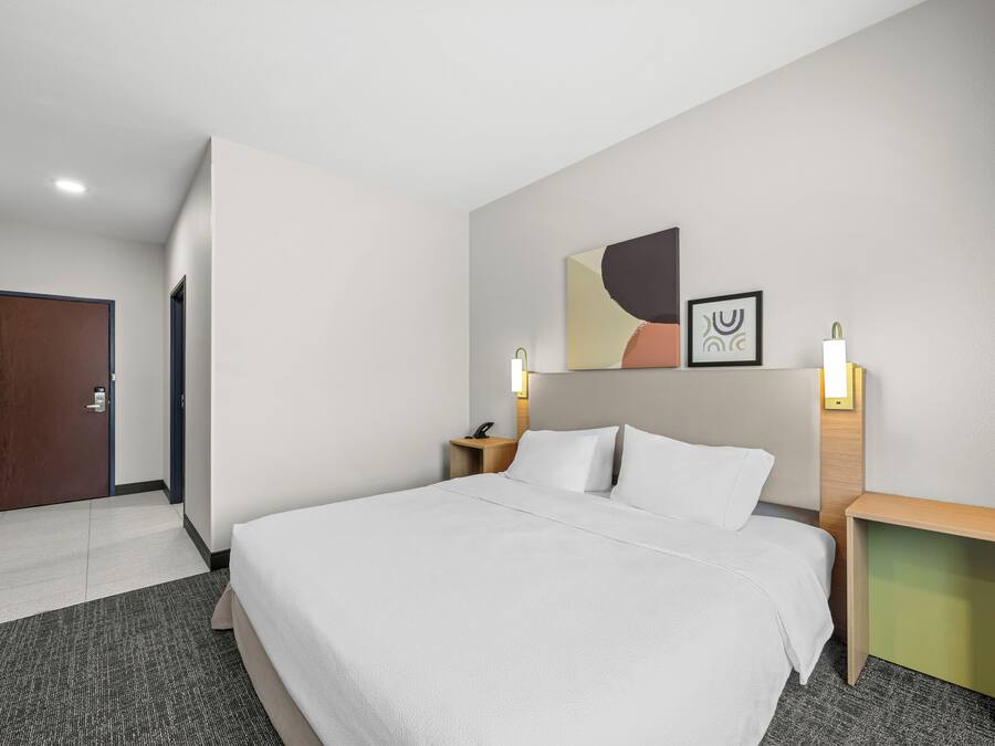 A hotel room with a bed, a nightstand, a wall-mounted lamp, and a door.