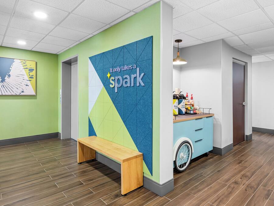 Een modern interieur met een groene wand, een blauwe accentmuur, een houten bank, een rolstoeltoegankelijke balie en een deur.