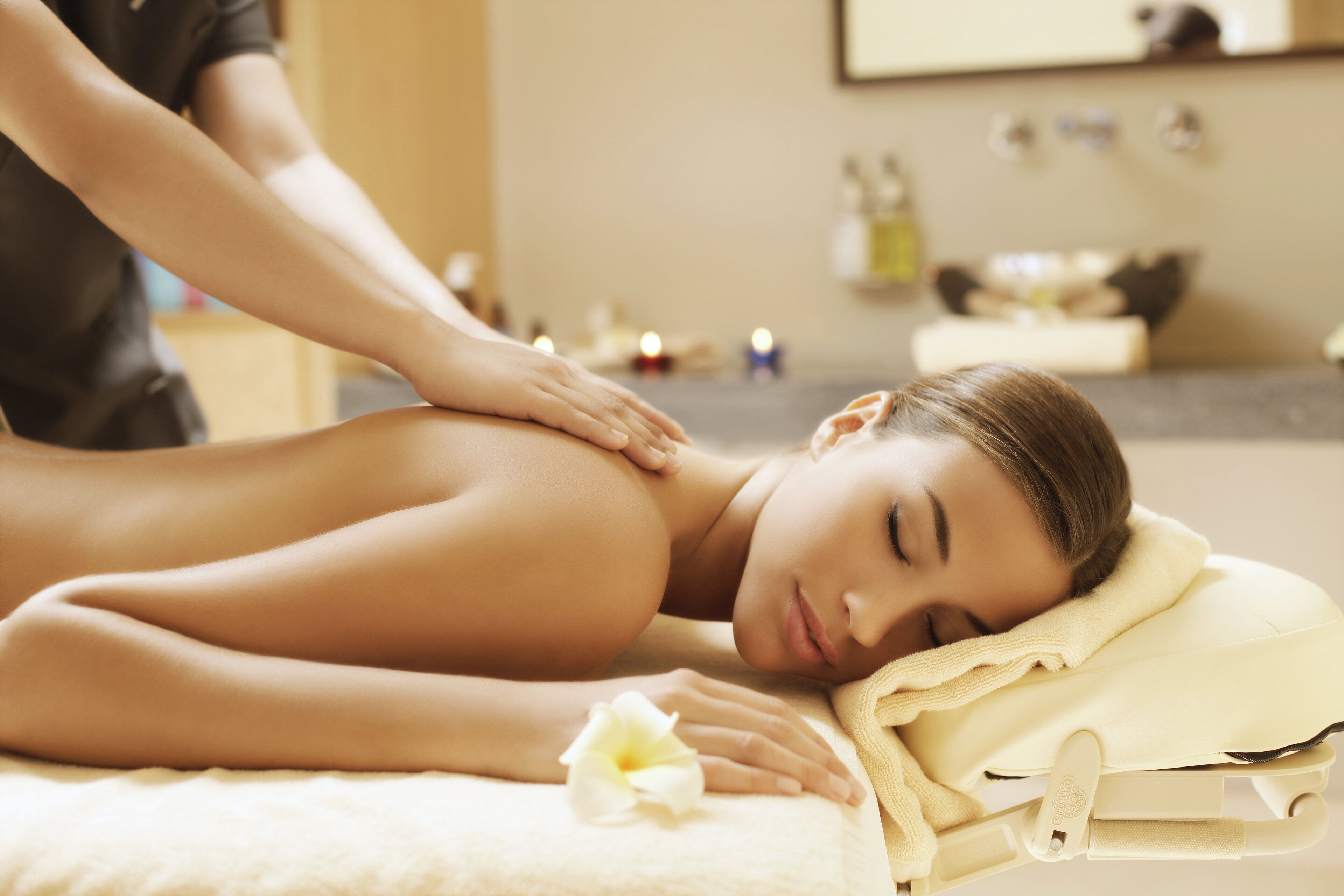 A massage therapy session in a spa setting with a client lying on a massage table, a therapist attending to the client, and a serene environment with candles and spa products in the background.