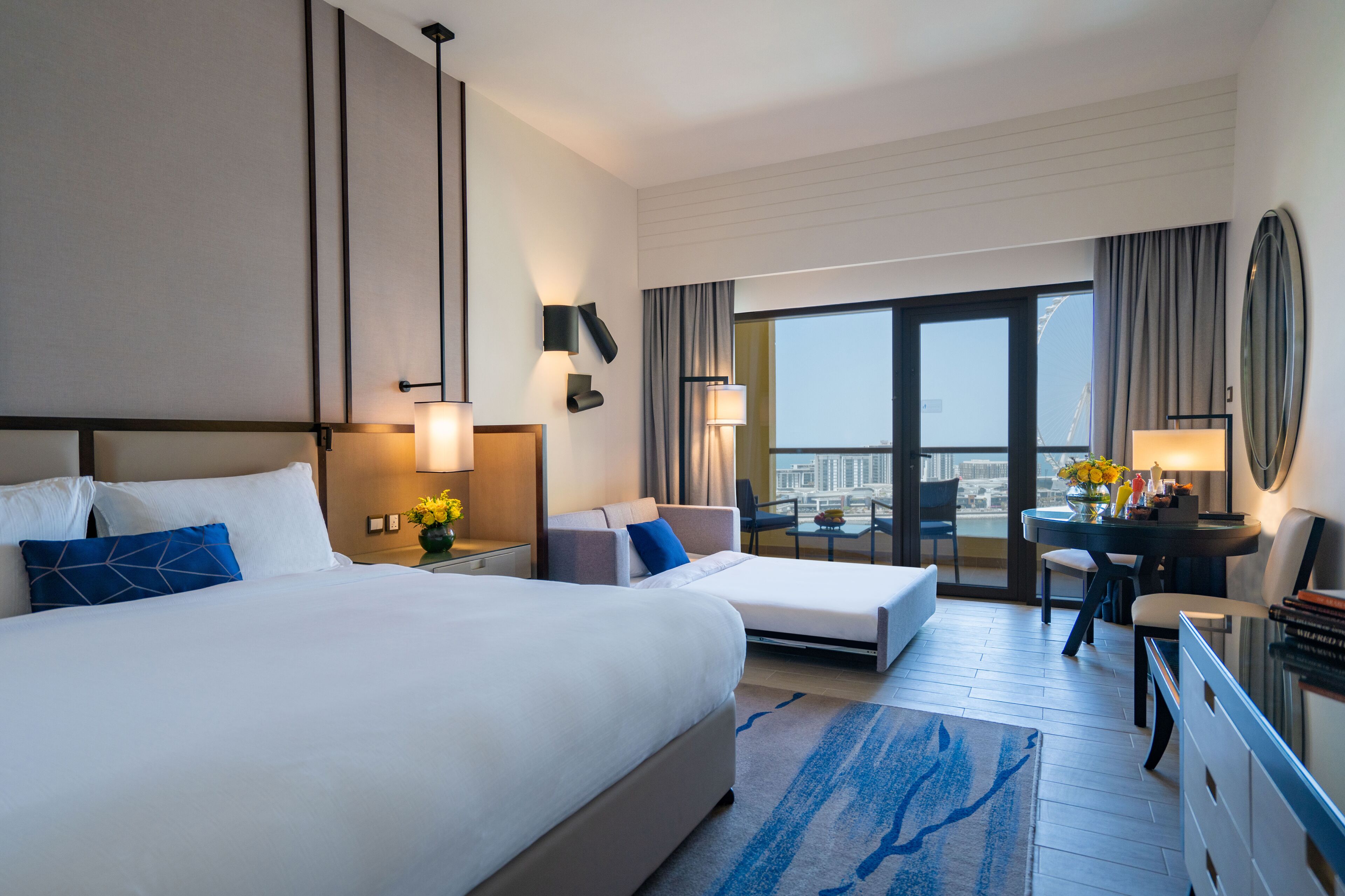 Habitación de hotel con dos camas, un escritorio, una silla y vistas a la ciudad.