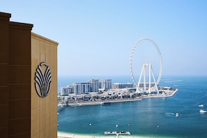 A coastal cityscape with a prominent Ferris wheel, high-rise buildings, and a beach. - Amwaj Rotana, Jumeirah Beach - Dubai (Dubai)