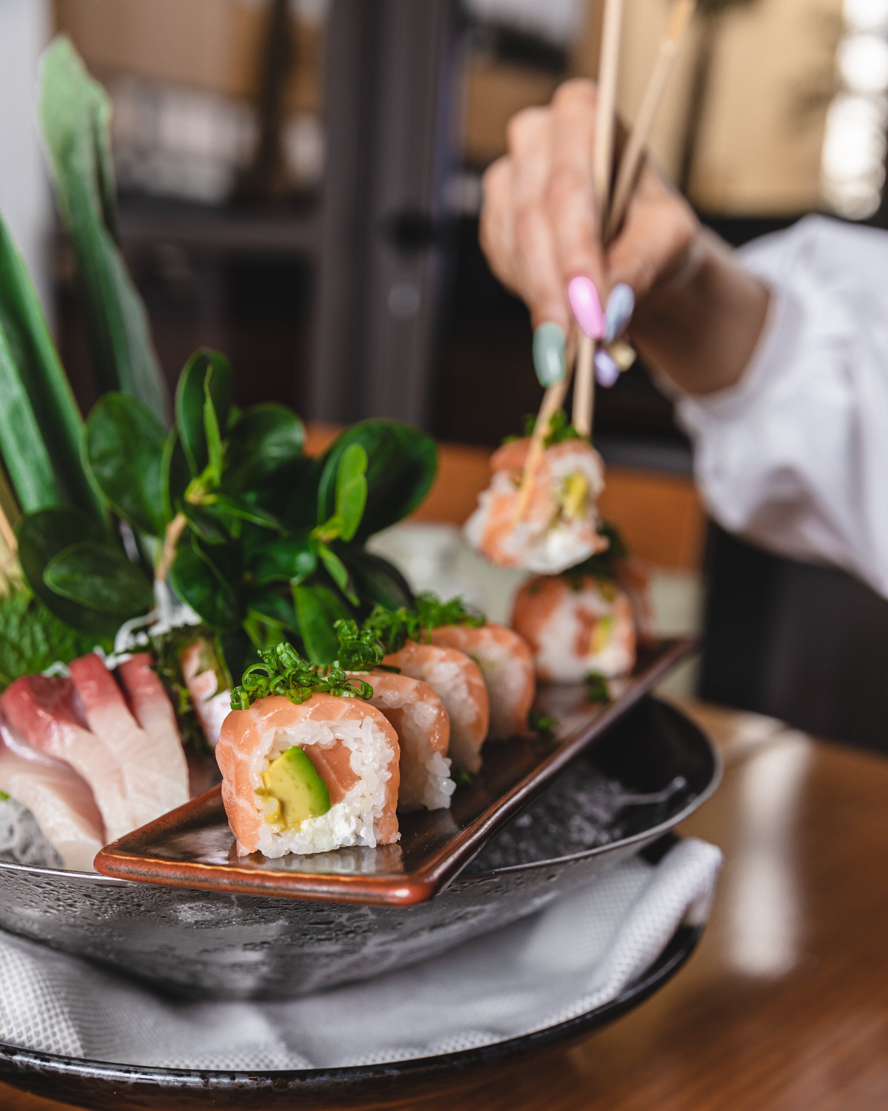 A sushi platter with various types of sushi, including salmon and avocado, on a black tray.