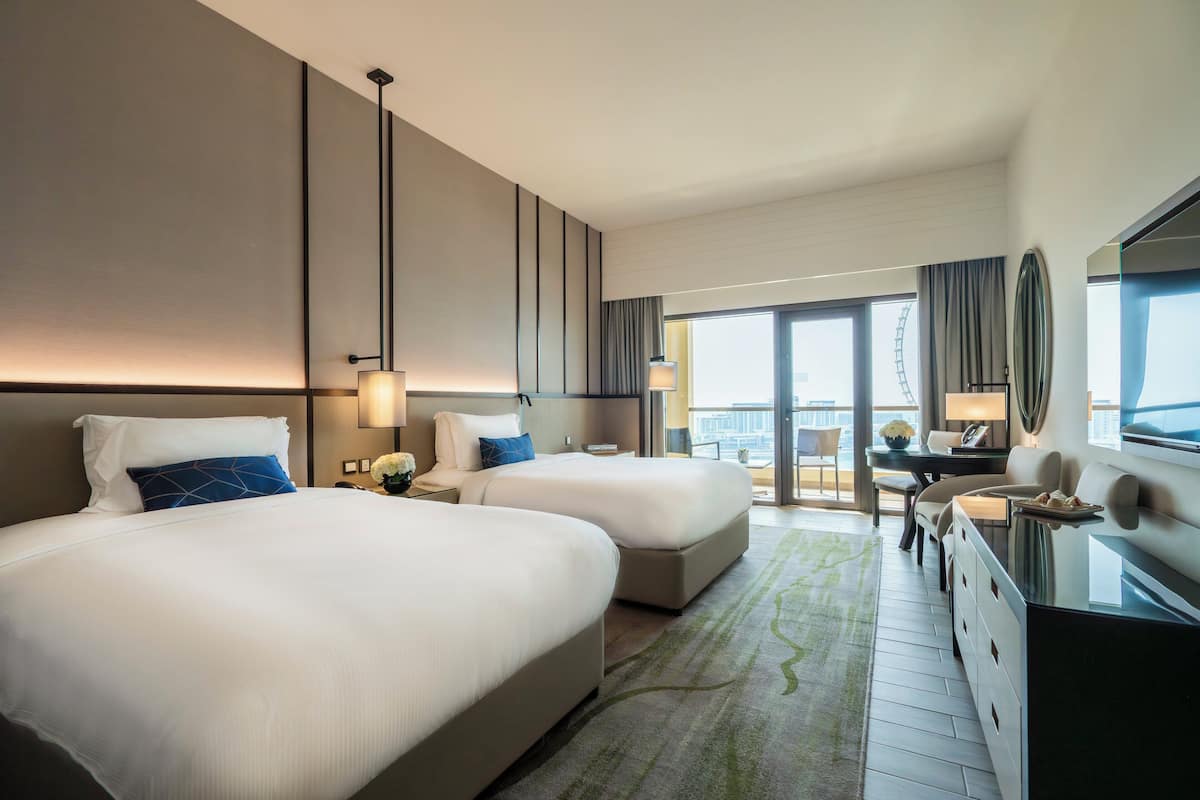 A hotel room with two beds, a desk, and a view of the city.