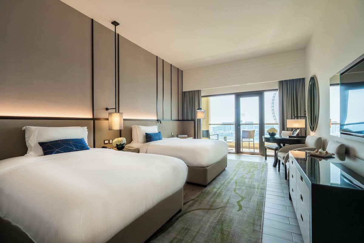 A hotel room with two beds, a desk, and a view of the city.