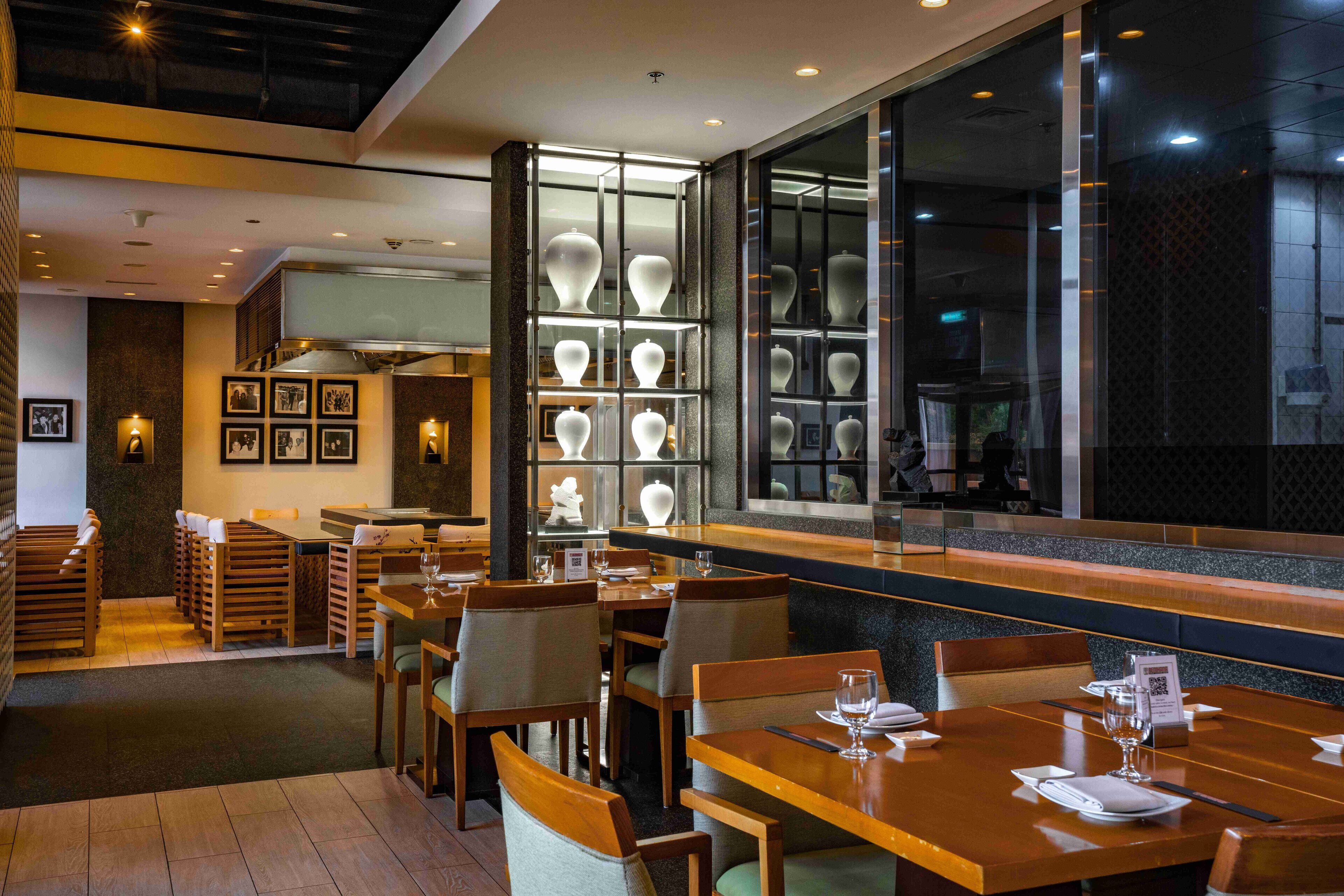 Un restaurante con mesas y sillas de madera, una vitrina de vidrio con jarrones y cuadros en la pared.