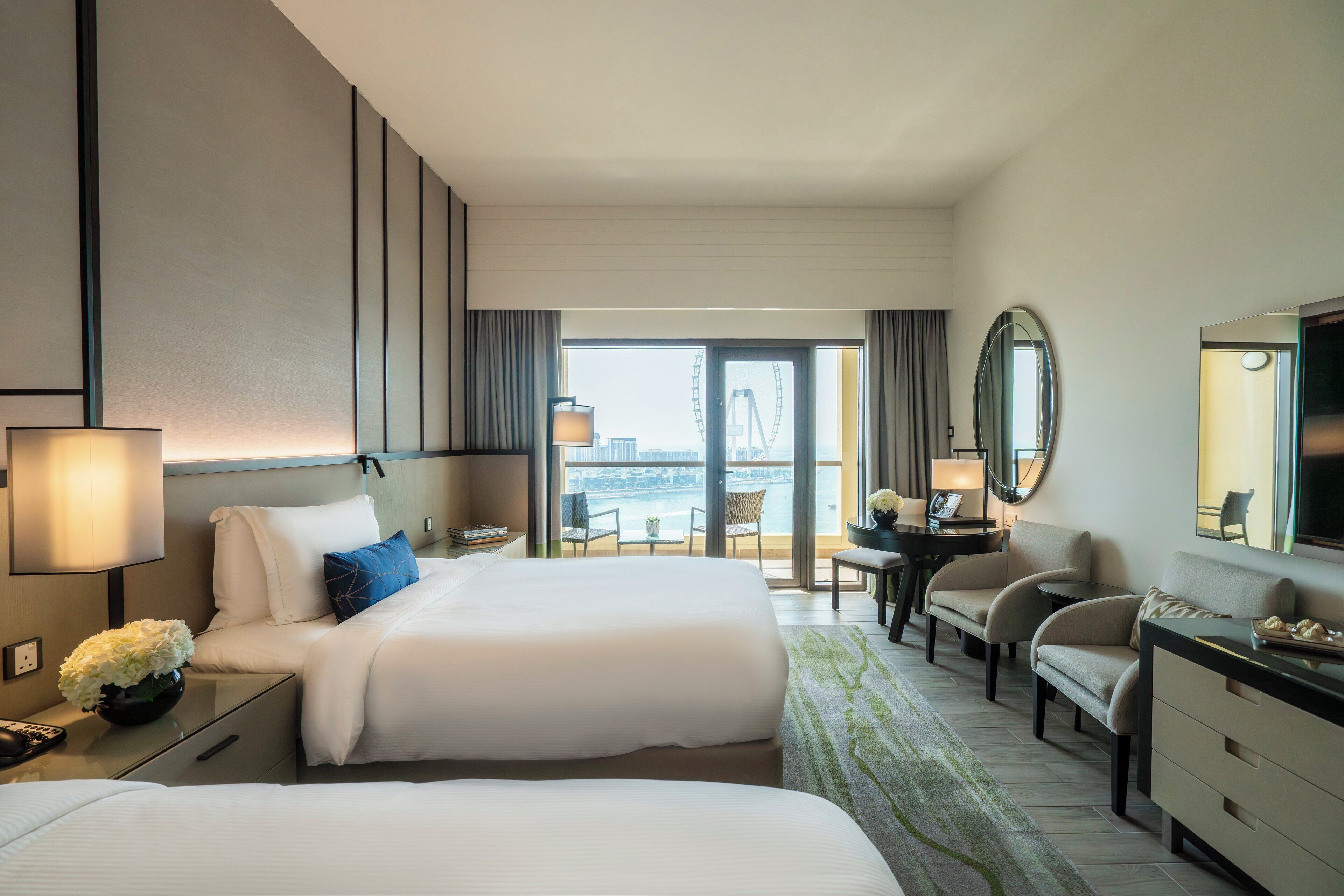 A hotel room with two beds, a desk, a chair, a TV, and a view of a Ferris wheel.