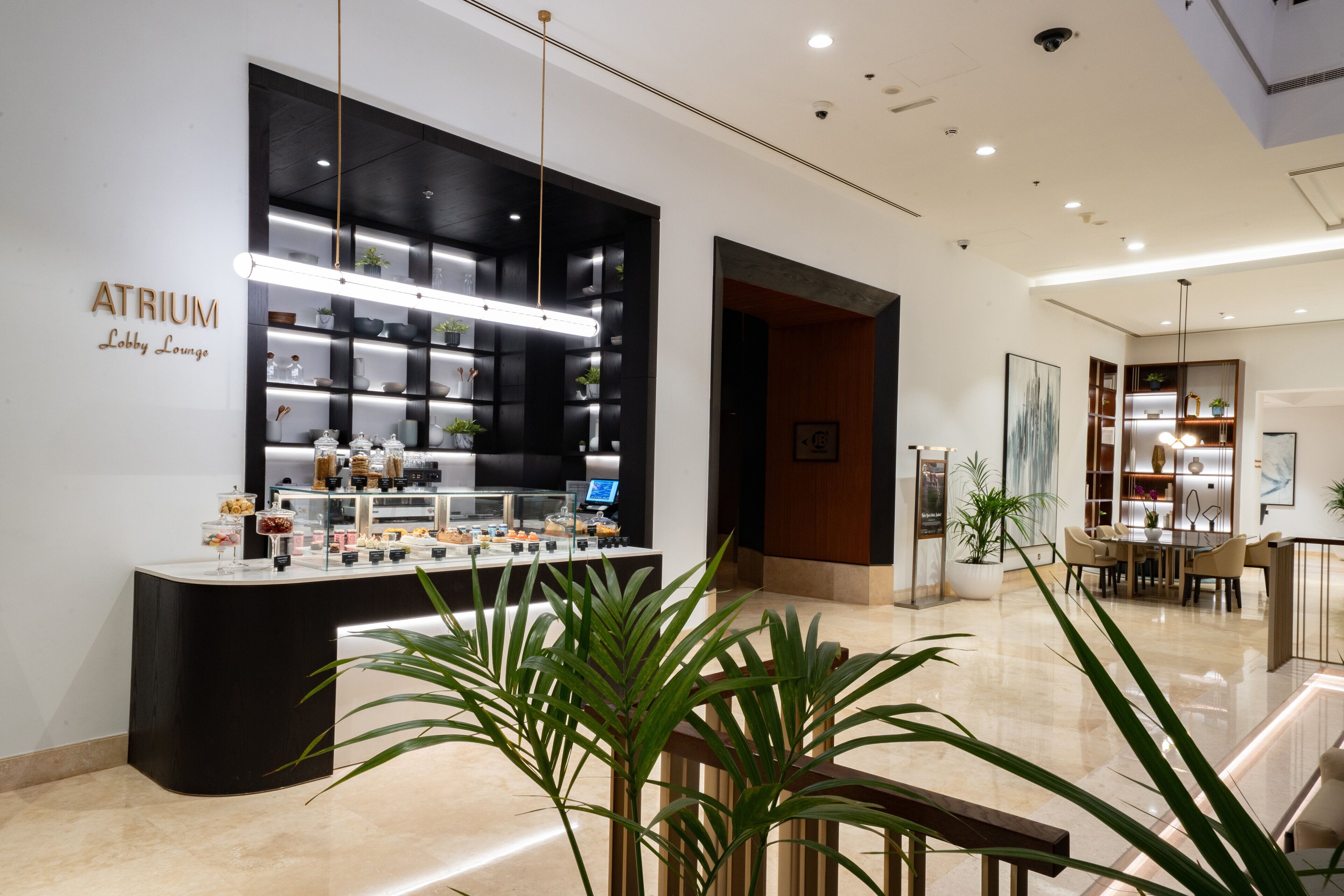 Un atrium moderne comprenant un bar à café, des étagères avec des plantes et un espace repas.