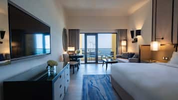 A hotel room with a large bed, a desk with a chair, a TV mounted on the wall, and a view of a bridge and water through the glass door.