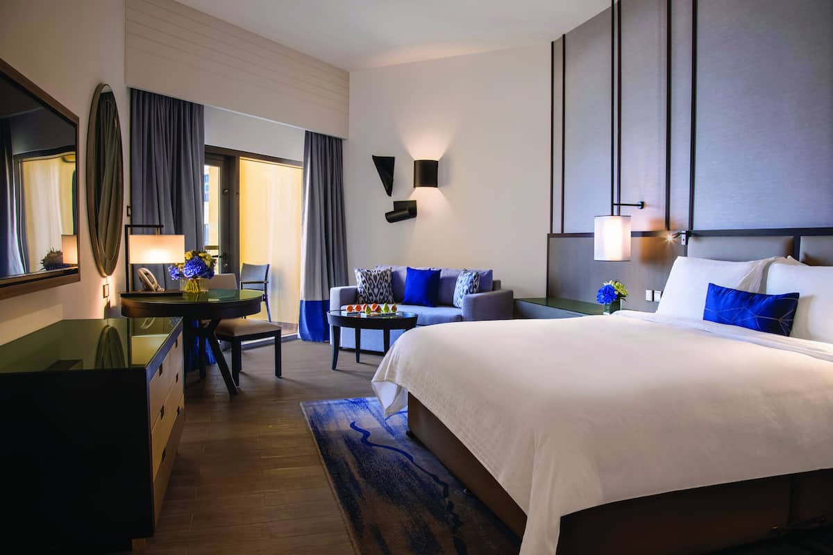 A hotel room with a large bed, a desk with a chair, a sofa, and a dining table.