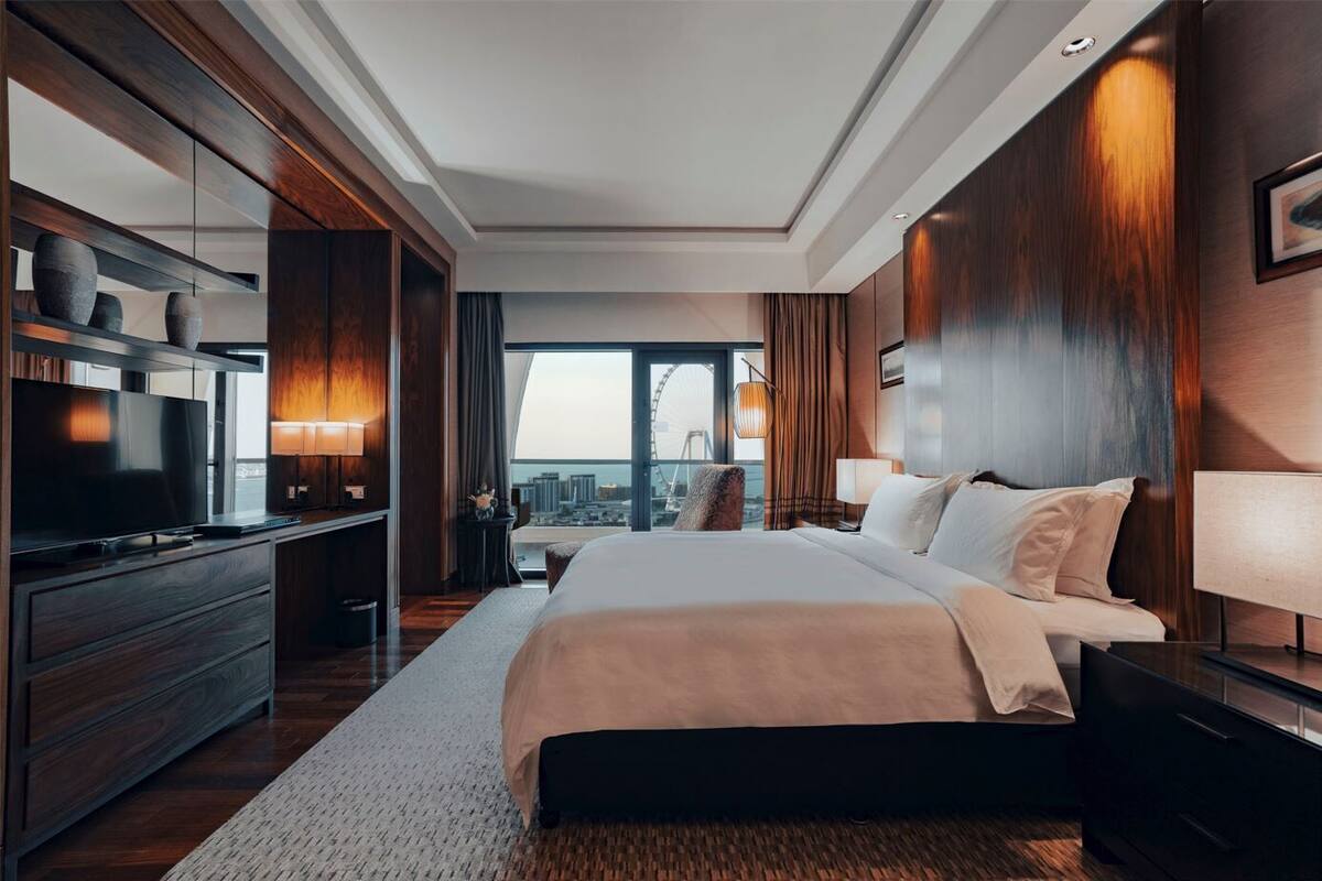 A modern hotel room with a large bed, a flat-screen TV, a desk, and a city view.