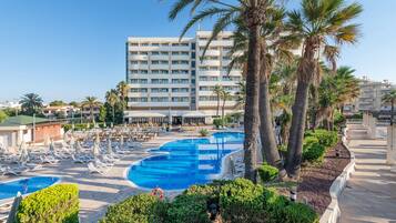 Un hotel con un amplio espacio de piscina, numerosas tumbonas y palmeras.