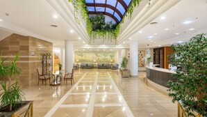 A spacious lobby with a high ceiling, a reception desk, seating area, and potted plants. - Welikehotel Marfil Playa (Sa Coma)