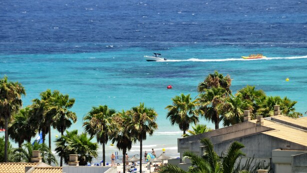A coastal view with palm trees, a beach, and a speedboat in the water. - Welikehotel Marfil Playa (Sa Coma)