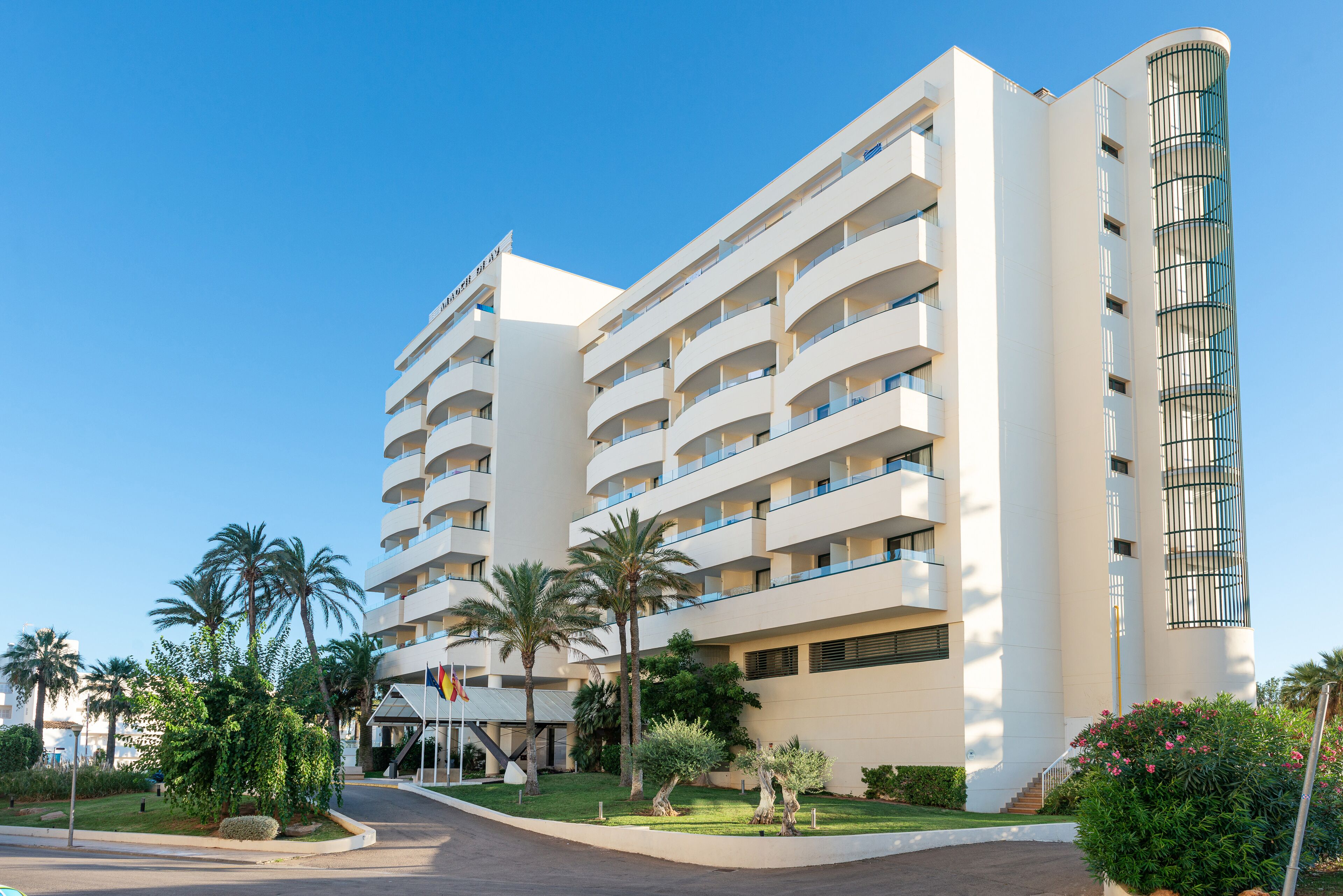 Un hotel de varios pisos con balcones, palmeras y un cielo despejado.