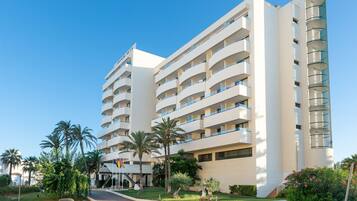 Un hotel de varios pisos con balcones, palmeras y un cielo despejado.
