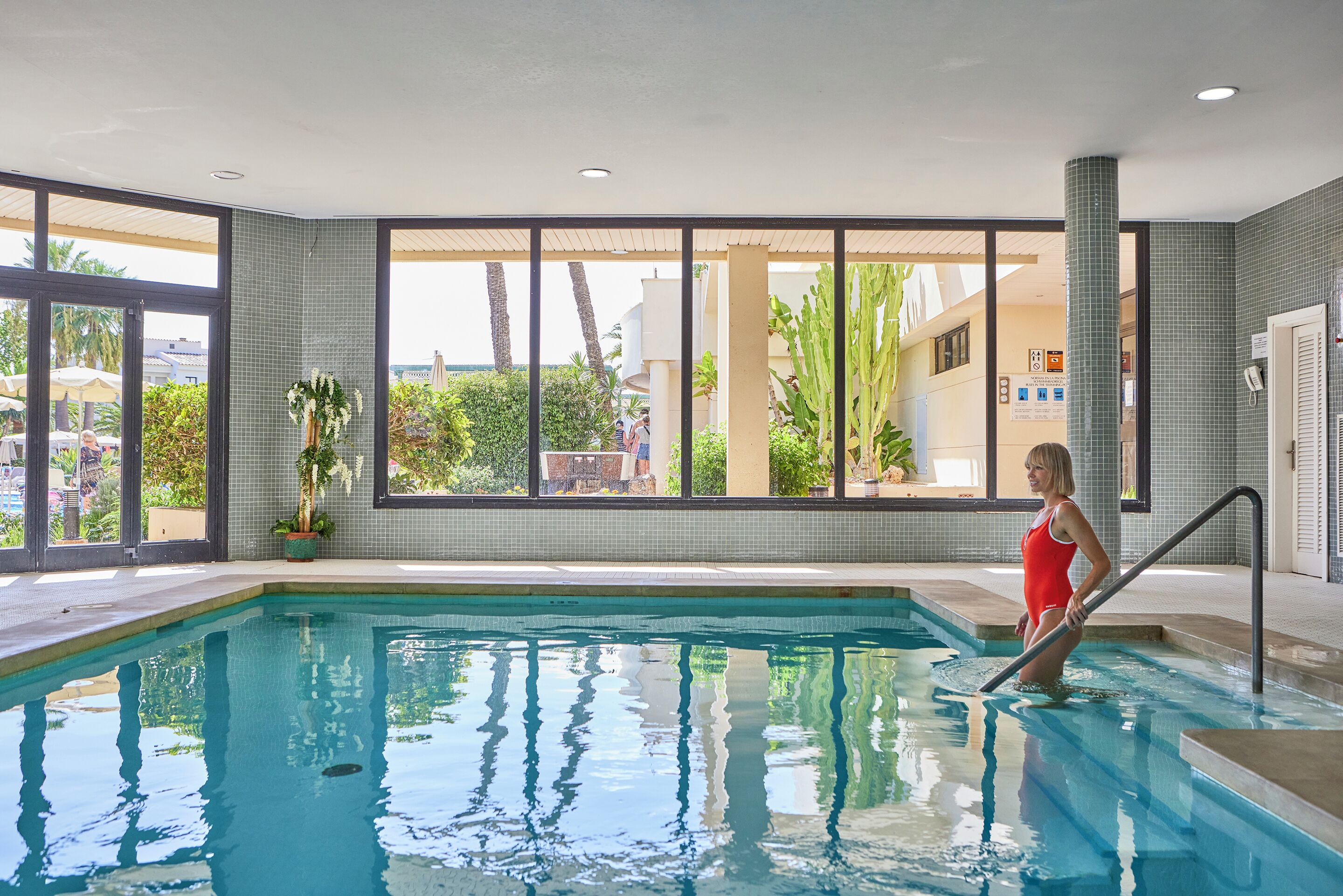 Una piscina interior con paredes de vidrio transparente, una escalera de piscina y vistas al exterior.