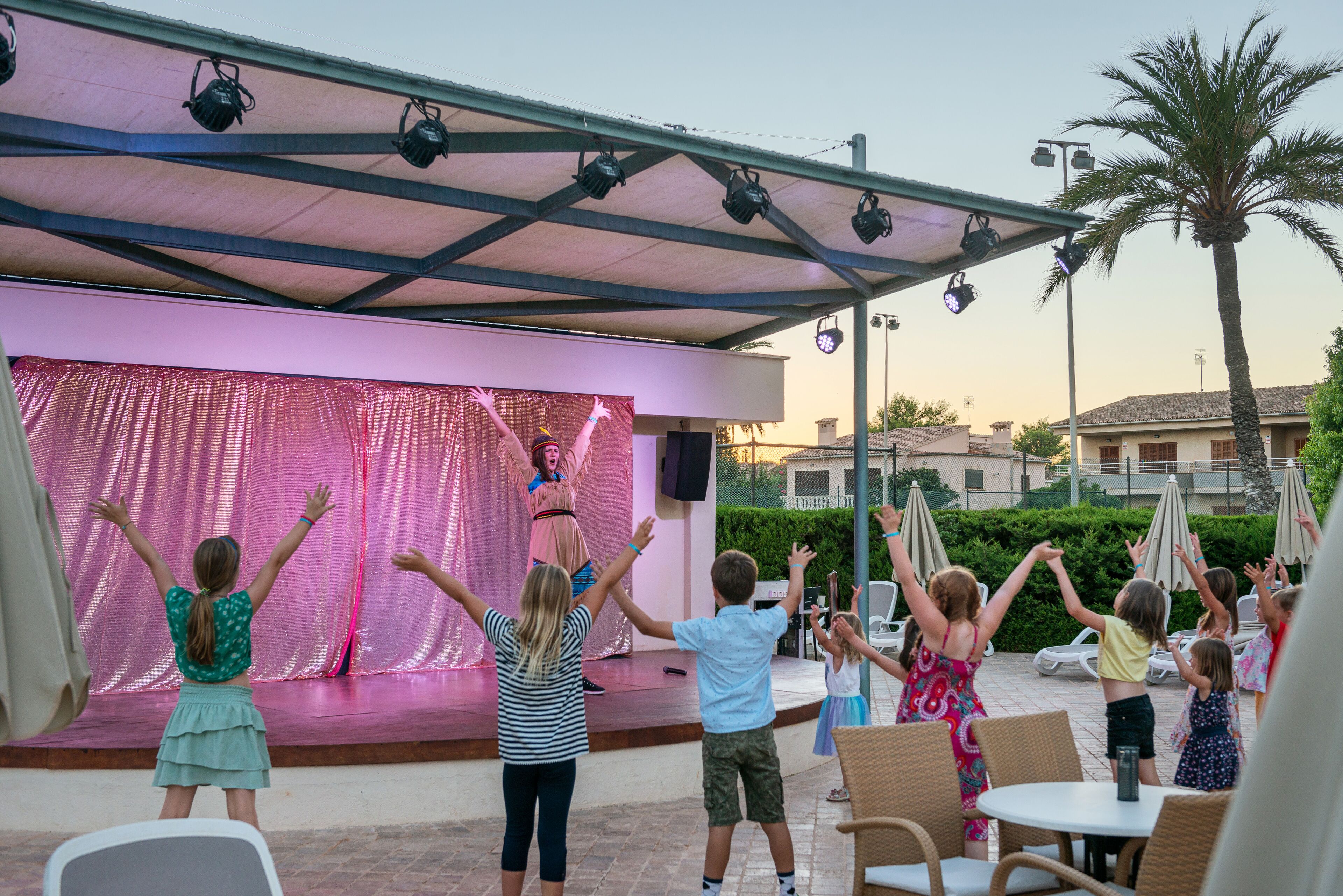 A stage with a pink backdrop and a performer, surrounded by an audience of children and adults.