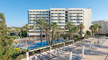 Un hotel con zona de piscina, palmeras y un cielo azul despejado.