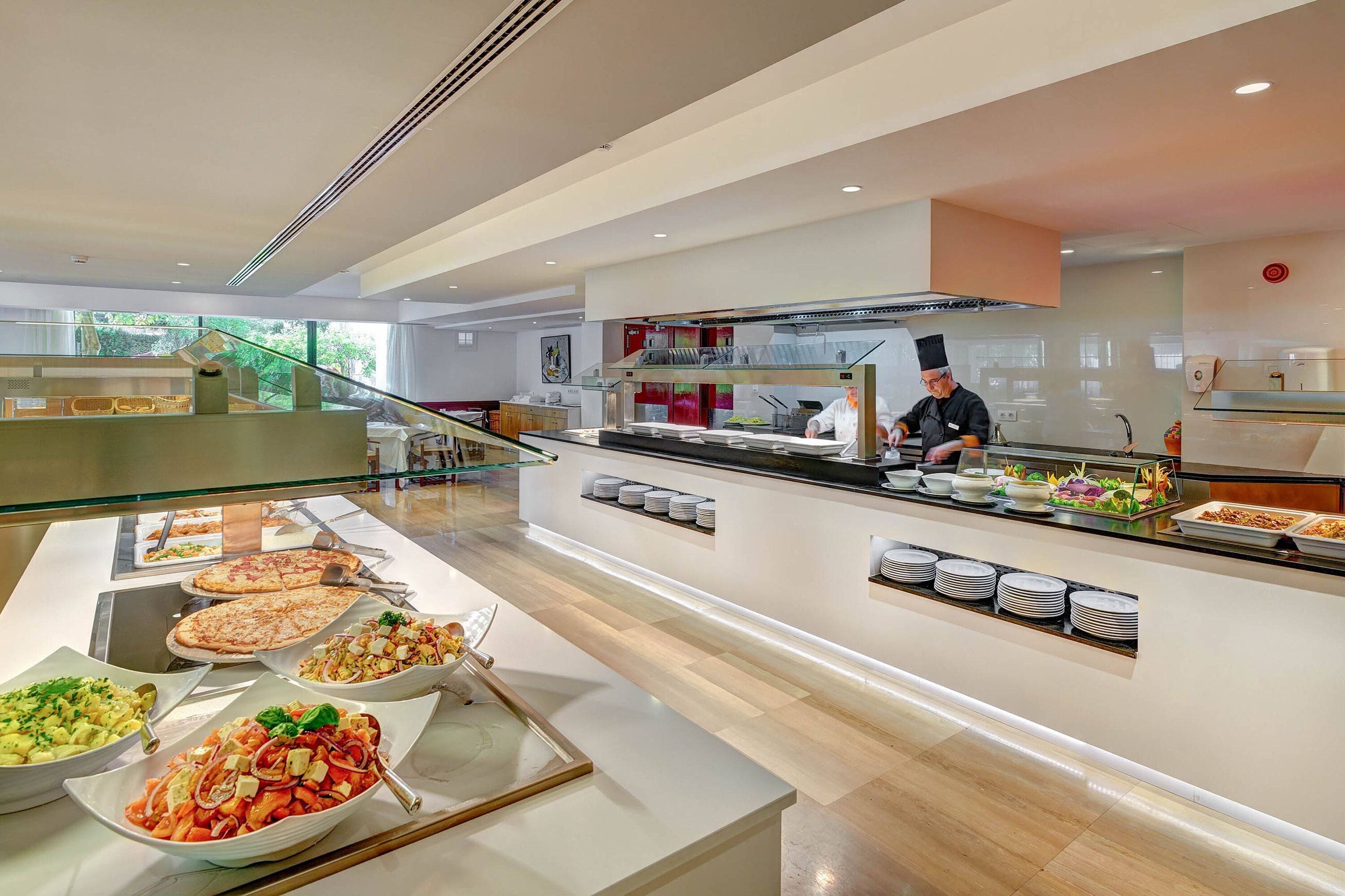 Zona de buffet con diversas opciones de comida, un chef preparando alimentos y una decoración interior moderna.