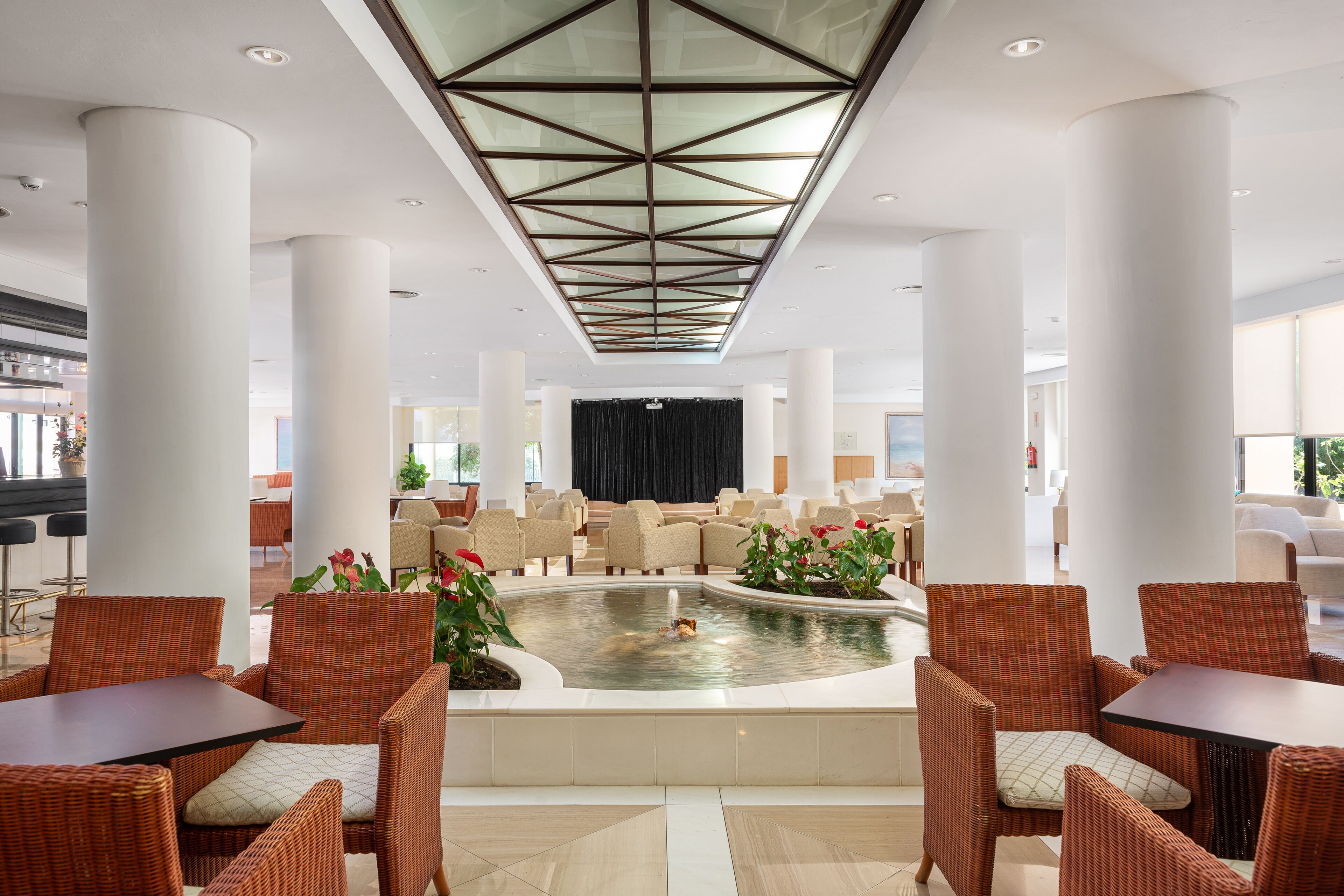 A lobby with a central water feature, seating areas, and a stage in the background.