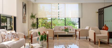 A spacious living room with a sofa, armchairs, a coffee table, and a large window offering a view of greenery.